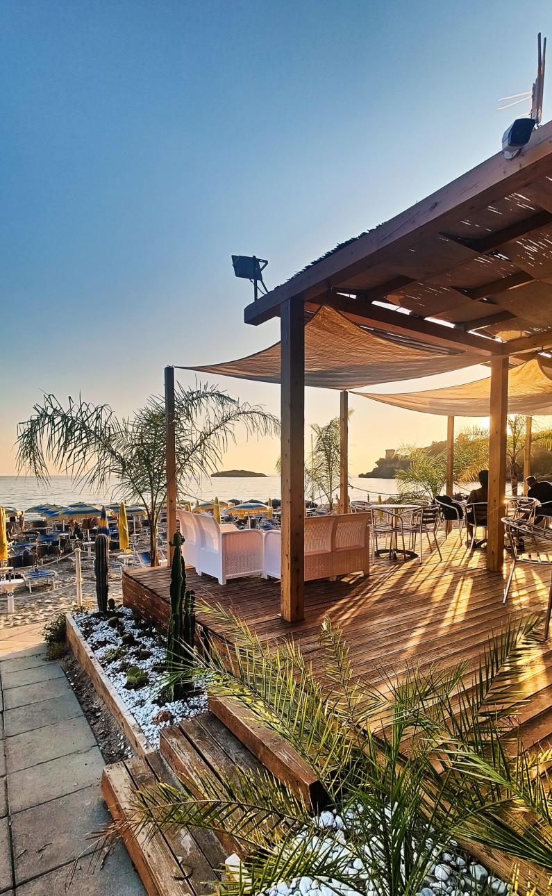 Seaside terrace with palm trees and chairs at sunset.